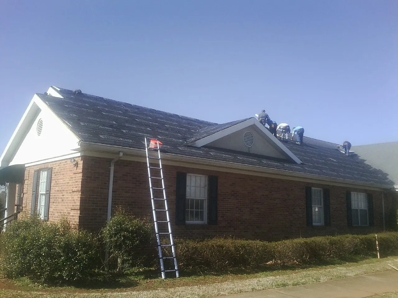 Crew tearing shingles off a brick ranch roof with a ladder set — Metal Roof Repair work by our crew in Greensburg