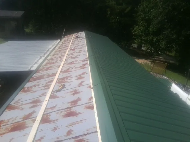 Old rusted panels beside newly installed green metal roofing — Wind Damage Roof Repair by Roofing Brothers in Greensburg