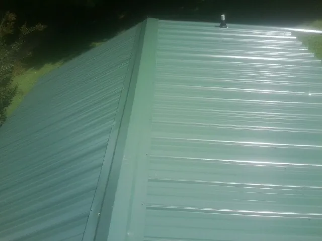 New green metal panels meeting at the ridge of a roof — Flat Roof Repair work by our crew in Greensburg