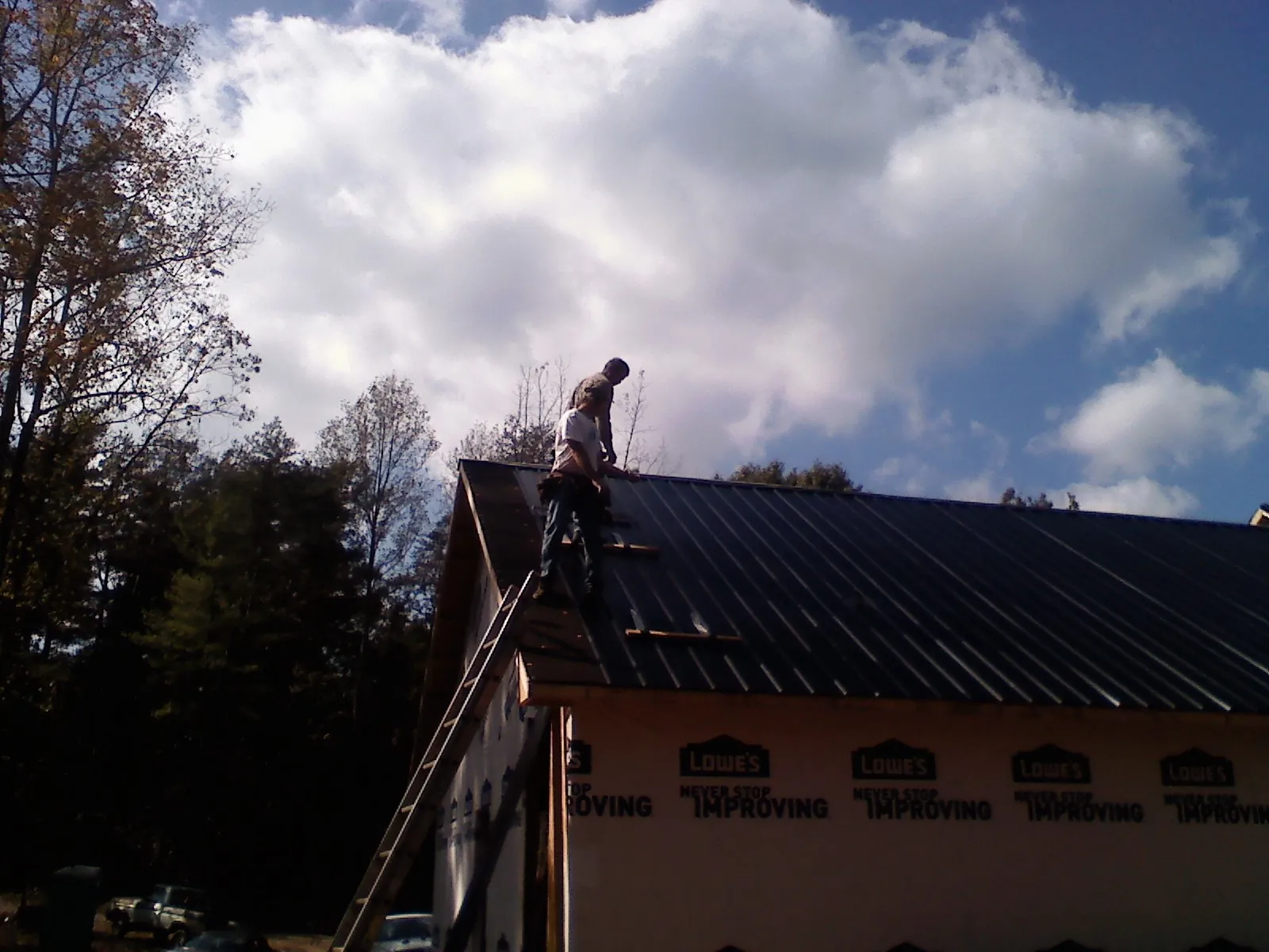 Roofer fastening dark metal panels high against a cloudy sky, from a Roof Inspection job in Greensburg